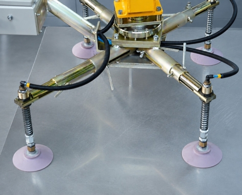 Detailansicht eines Vakuumsaugers für Bleche mit Saugtraverse, Saugnäpfen und Vakuumleitungen auf einer glatten Metallplatte.
