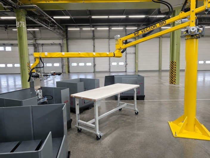 Vakuumsauger Bleche an einem gelben Schwenkarm-Vakuumheber für das ergonomische Handling von Bauteilen an Sortierbehältern in der Industriehalle.