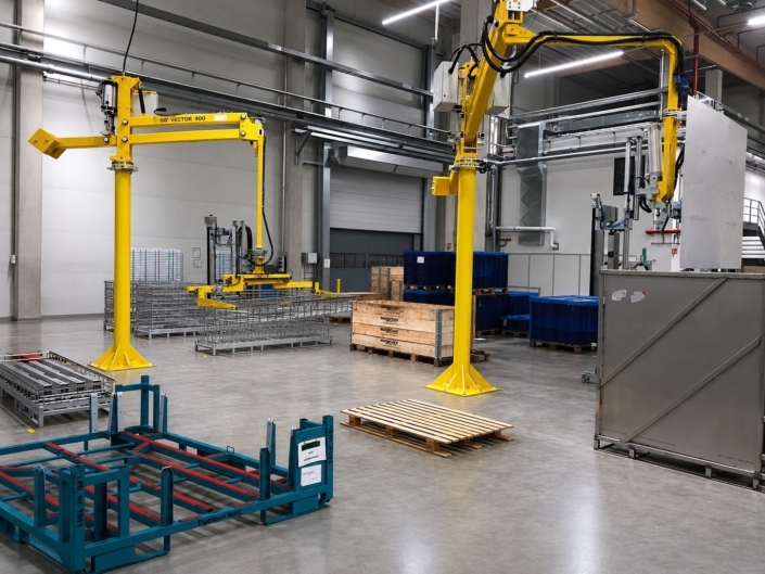 Vakuumsauger Bleche an mehreren gelben Schwenkarm-Vakuumhebern ermöglichen das ergonomische Handling von Bauteilen in einer modernen Fertigungshalle.